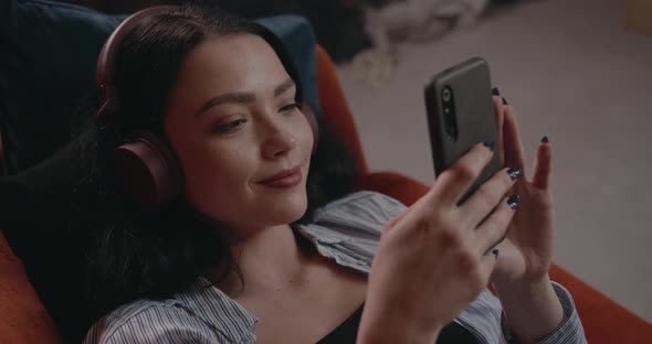 The Girl Listens To Music and Views the News on Her Phone While Lying on the Couch alt
