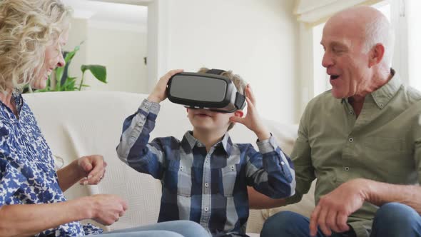 Happy senior caucasian couple with grandson using vr headset in living room alt