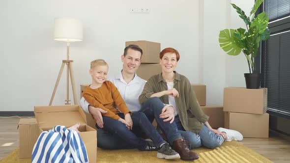 Portrait Of Caucasian Family With Child Boy Sitting On Floor In New Apartment Looking At Camera