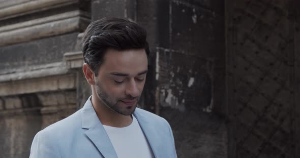 Young Man Rides Near The Ancient Castle In A Festive Light Suit And Talks On The Phone alt