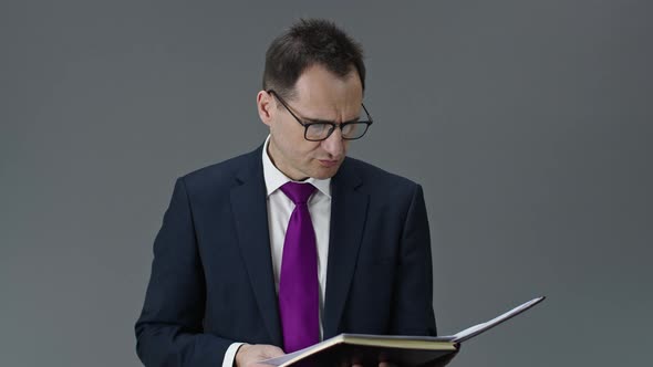 Handsome Entrepreneur Checks Notes in Daily Planner, Seriously Looks at Camera alt