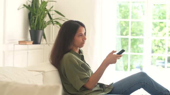 Indian Woman Sits on the Sofa at Home and Holds Remote Control Watching TV