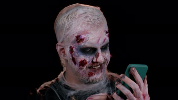Frightening Man Halloween Zombie Using Mobile Phone Typing New Post on Web Browsing Addiction alt