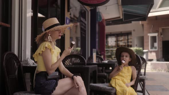 Mother and Daughter Eating Icecream at the Street Cafe in Summer Day alt