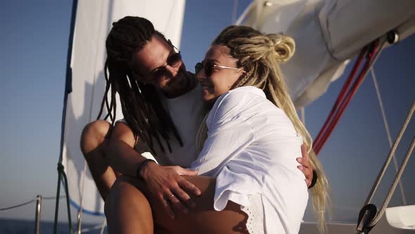 Low Angle Footage of Stylish Couple with Dreadlocks in White Clothes and Sunglasses Sitting alt