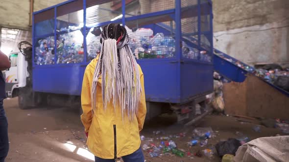 Backside Footage of a Woman with Dreadlocks Wearing Yellow Jacket Watching the Process on Waste alt