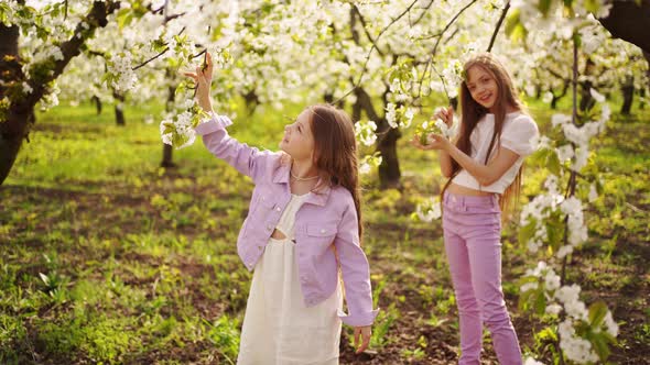 Two Longhaired Girls Sisters Walk in the Garden with Flowering Trees alt