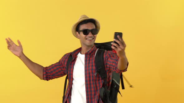 Indian tourist man with backpack smiling and waving bye while having video call on mobile phone