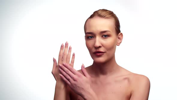 Beautiful Woman Rubs Drop of Cosmetic Cream on Hand While Looking at Camera White Background in alt