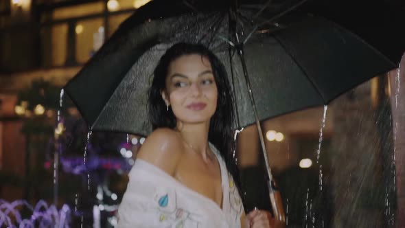 Portrait of Wet Brunette Stands Under Black Umbrella During Night Rain alt