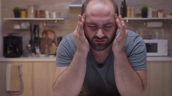 Man with Headaches Sitting in the Kitchen alt