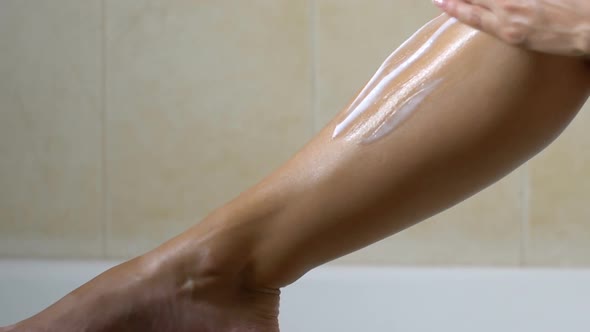 Woman Applying Lotion After Waxing Legs in Bathroom, Hair Removal and Skin Care alt