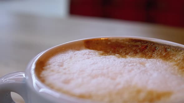 Cup of Cappuccino with White Foam on the Wooden Table in the Restaurant. Close-up alt