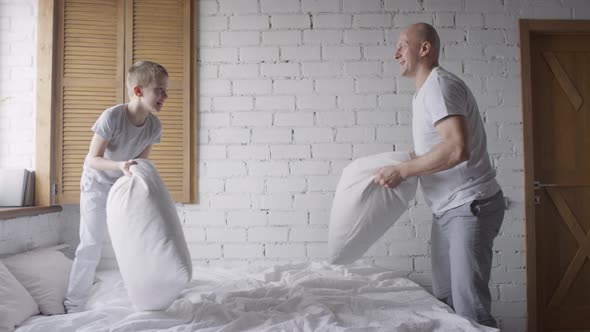 Happy Little Boy and his Father Pillow Fighting in Morning alt