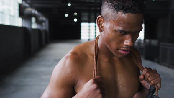 Shirtless african american man tired after skipping the rope in an empty urban building alt