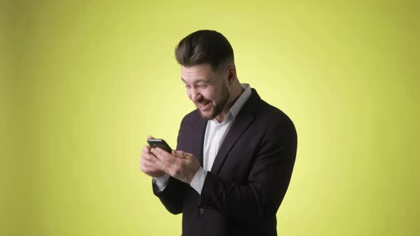 Worried Young Man in Office Suit Looking on Smartphone Doing Winner Gesture