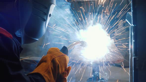 Worker welding a piece of metal. Sparks, strong light. Worker using a special helmet as a protection alt
