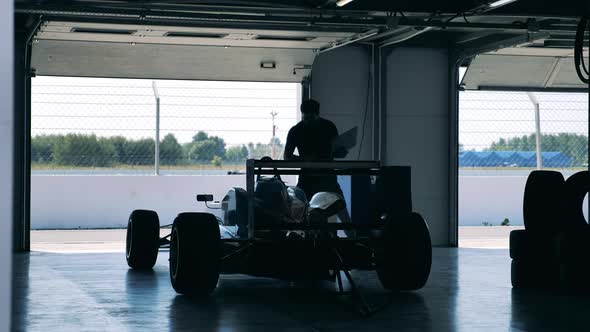 A Man with a Laptop is Inspecting a Racing Car alt