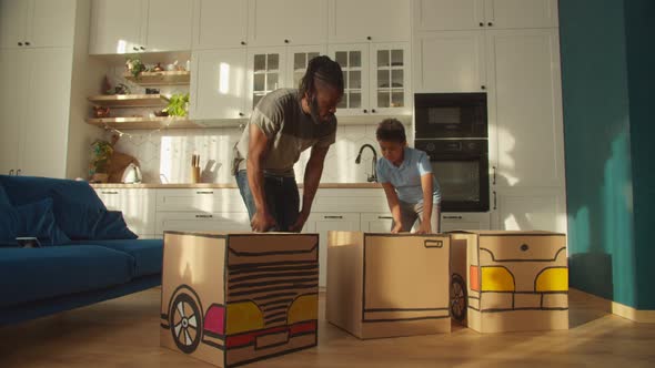 Cute African American Son and Father Making Toy Cardboard Car at Home alt