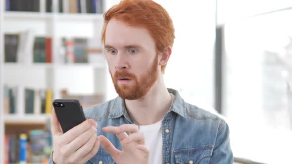 Casual Redhead Man Shocked By Results on Phone alt