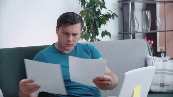 A man is concentrating on documents while sitting on the couch at home