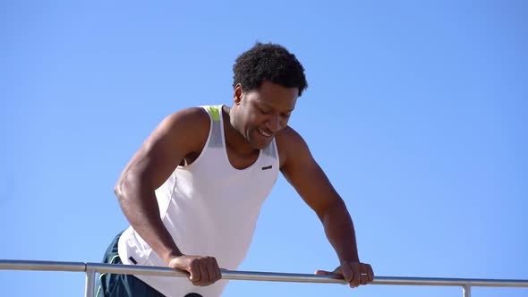 Happy Muscular Man Doing Push Ups on Bar Against Blue Sky alt