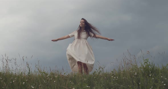 Young Woman in Feminine Dress Turning Around Outdoors on Green Field Before Rain Starts. Happy Girl