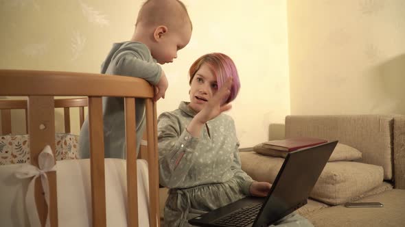 A Woman is Talking By Video Call Using Laptop and Her Son is Watching on It Standing in His Crib alt