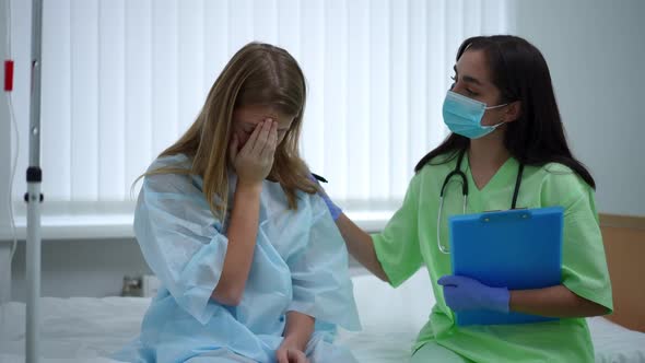 Teenage Girl Crying Sitting on Bed with Doctor Touching Shoulder Endorsing Patient alt