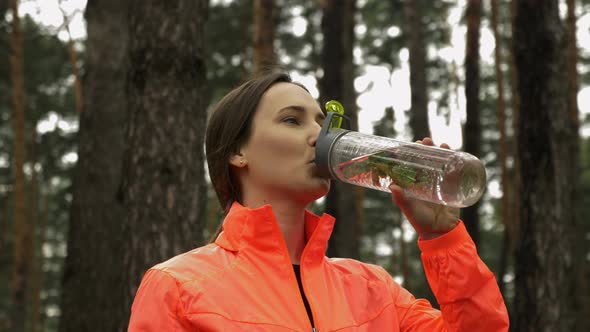 Young woman drinking water in the park. Female athlete drinking water after running alt