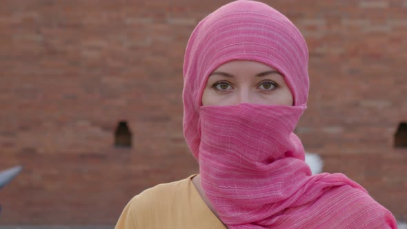Attractive Muslim Woman with Natural Make Up Wearing Pink Hijab Scarf Looks at Camera alt