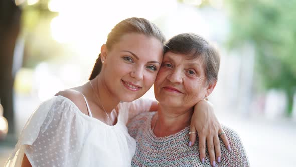 Beautiful Portrait of Grandmother and Her Granddaughter Standing Outdoor on Summer Street alt