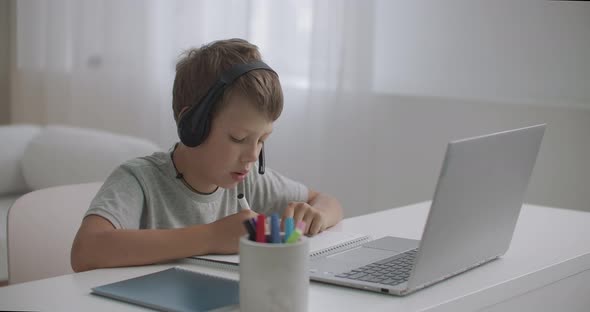 Little Boy Is Watching Educational Videos for Children on Laptop and Listening By Headphones alt