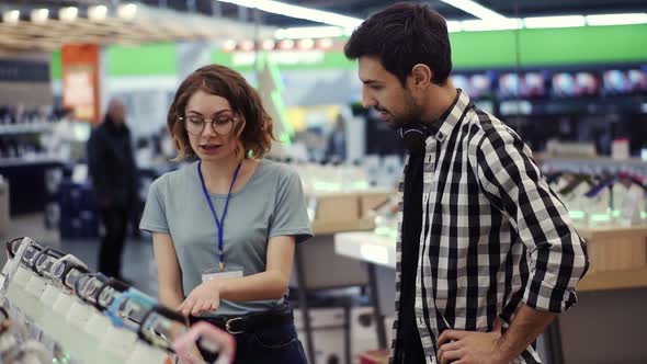 In the Electronics Store Female Consultant Gives Professional Advice to a Young Man alt