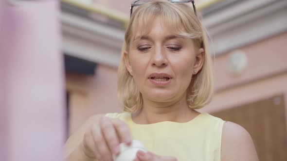 Close-up of Satisfied Blond Woman Smelling Moisturizer on City Street Outdoors. Portrait of alt