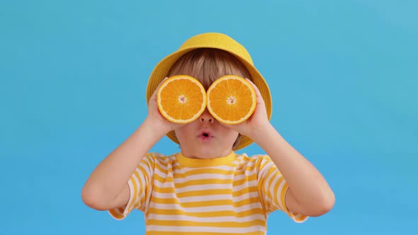 Surprised child holding halves of orange fruit like a sunglasses