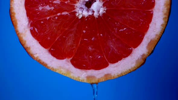 Juicy Pulp of Fresh Red Grapefruit in Blue Background Fresh Water or Juice is Flowing From Slice alt