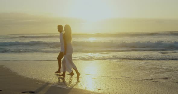 Couple walking together on beach during sunset 