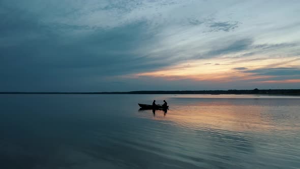 Silhouettes of Two Fishermen Sailing on a Small Boat at Sunset alt