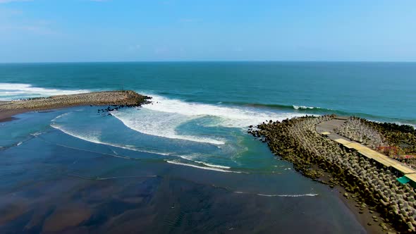 Black sand Glagah Beach lagoon, ocean waves crush on breakwater, Java, Indonesia alt