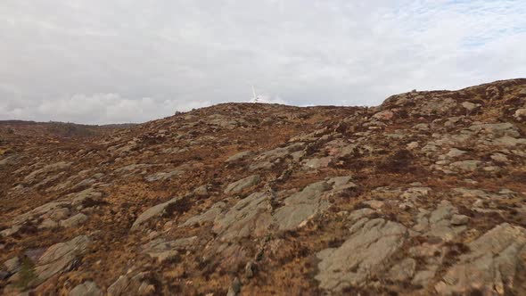 Flying up natural hillside and revealing two wind turbines behind hill at Lindesnes wind park in sou alt