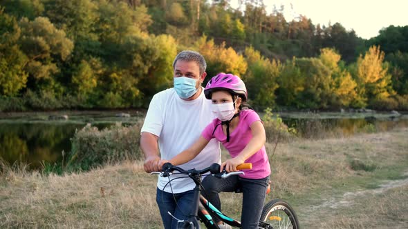 A bearded father teaches his daughter to ride a Bicycle in medical masks and a Bicycle helmet 