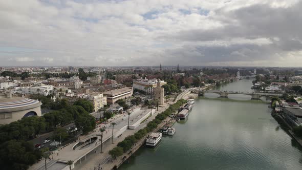 Drone flight over Guadalquivir river past Torre del Oro watchtower, Seville