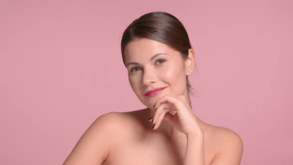 30s Brunette Woman Wears a Decollete Top with Ideal Skin in Studio on Pink Background Poses