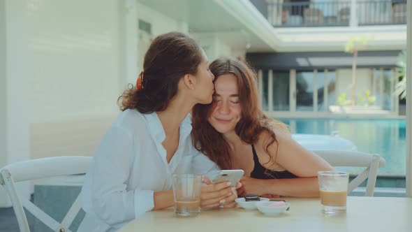 Happy Female Couple Using a Smartphone While Drinking Coffee alt