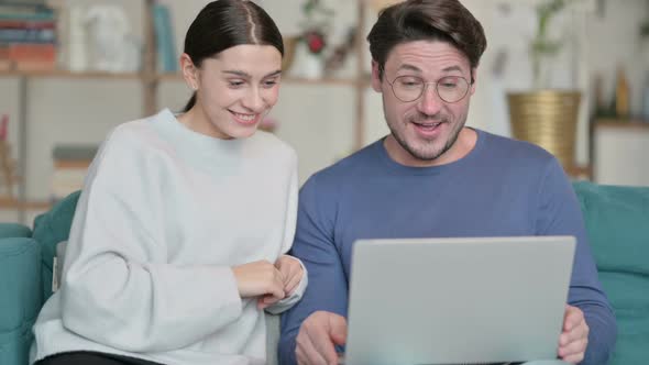 Online Video Call on Laptop By Hispanic Couple Sitting on Sofa alt