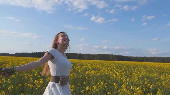 A Happy Girl Is Spinning Among a Rapeseed Field on a Warm Spring day.Slow Motion Mode. alt