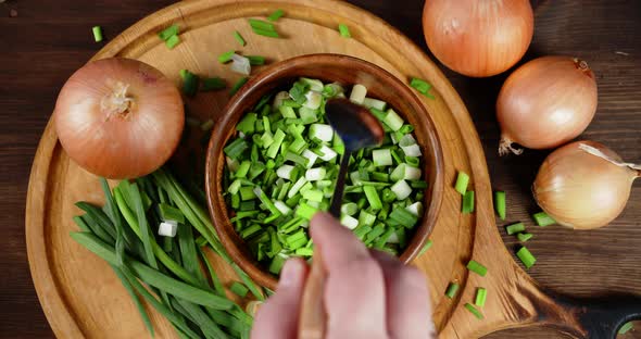Man's Hand with Spoon Mixes Chopped Green Onions in Bowl. 