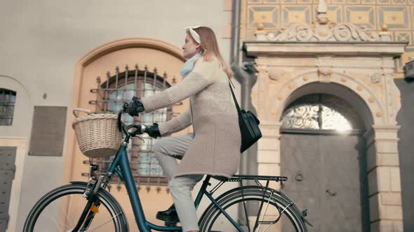 Woman in Coat Rides Bicycle in Old Street with Beautiful Buildings in Autumn