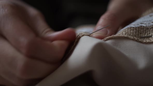 Closeup view of female hands sewing  jute linen stripe to beige cotton cloth. Boho rustic home decor